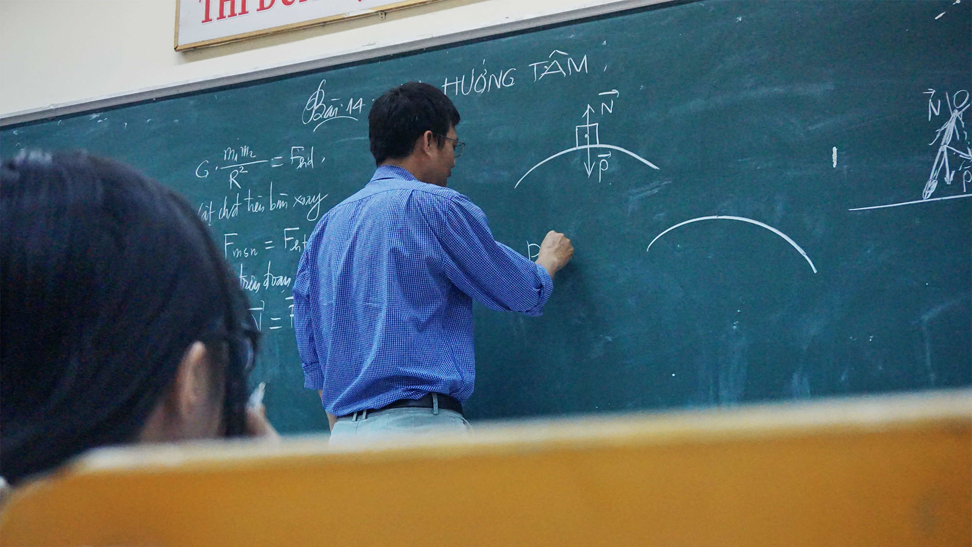 professor writing on chalk board in class room